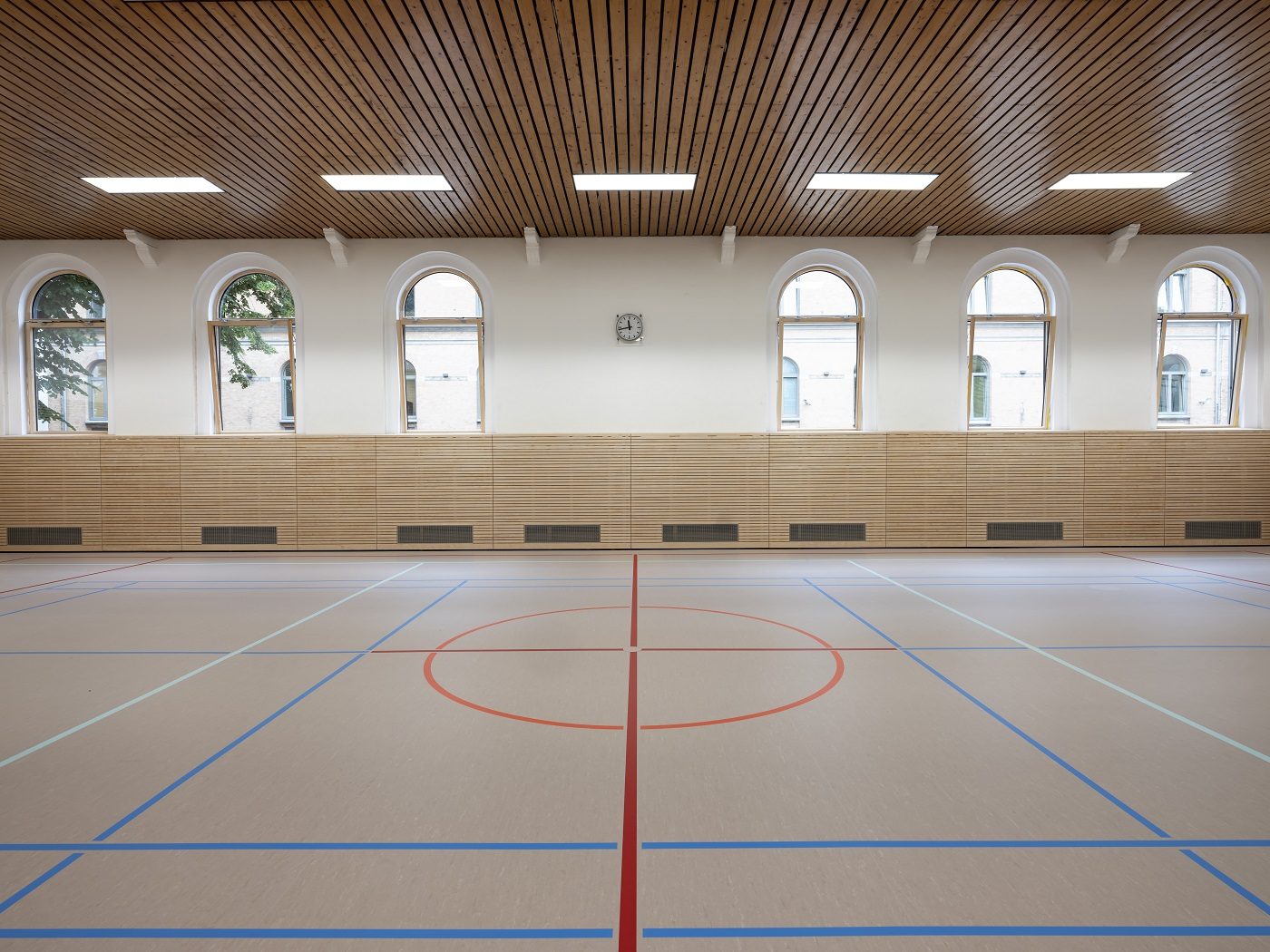 Sanierte Turnhalle mit Holzlamellenwänden und Rundbogenfenstern